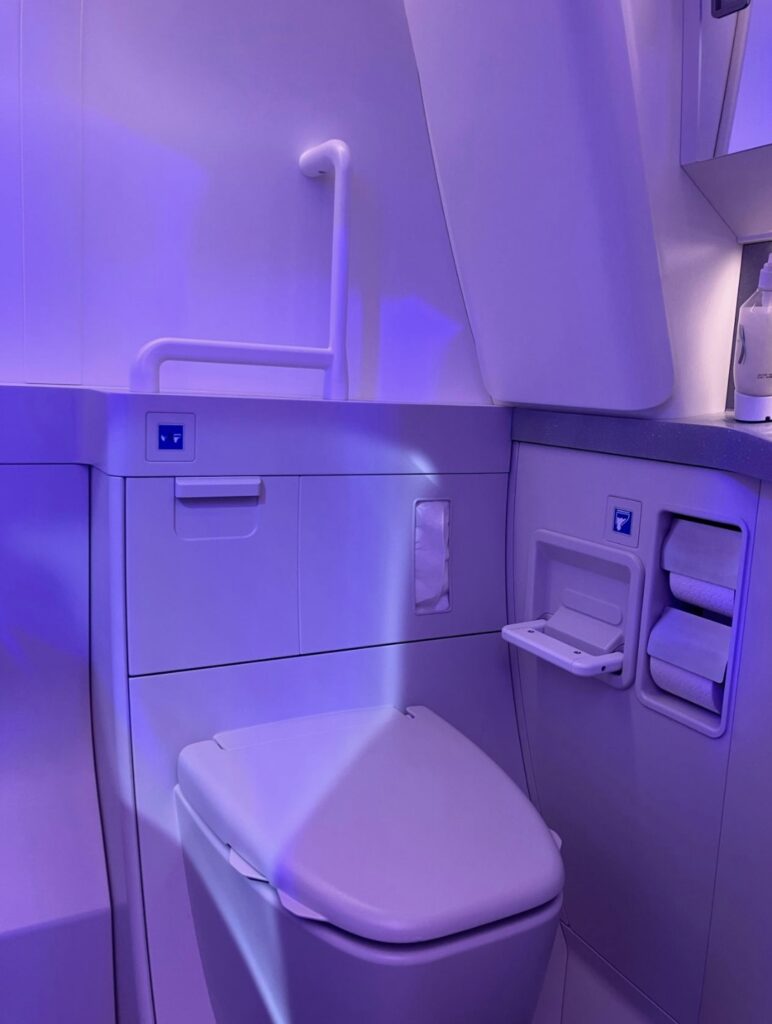 Collins Aerospace's accessible lavatory for Boeing aircraft, as seen on the Boeing stand. The space is flooded in purple LEDs and a prominent grab bar is in view above the toilet.
